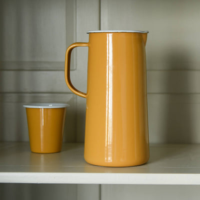 Yellow jug and cup made fro enamel on a shelf inside a dresser