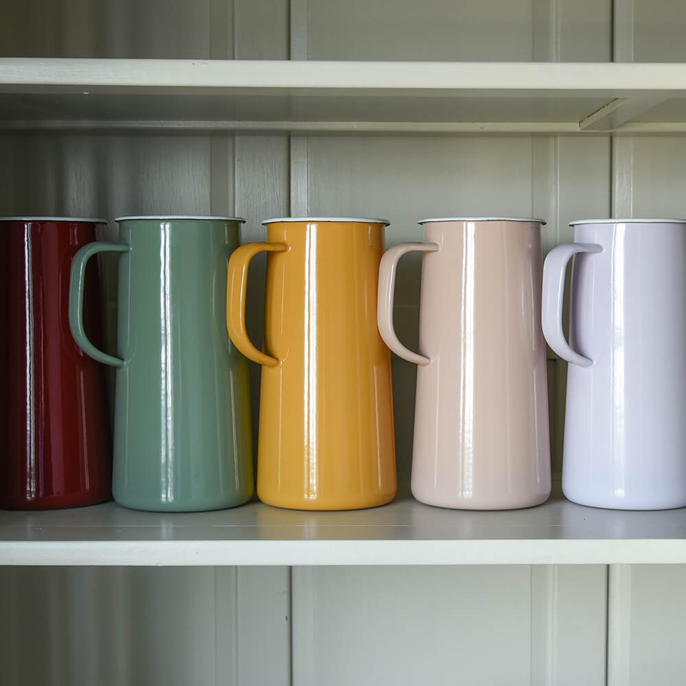 Row of colourful jugs made from enamel on a shelf inside a dresser
