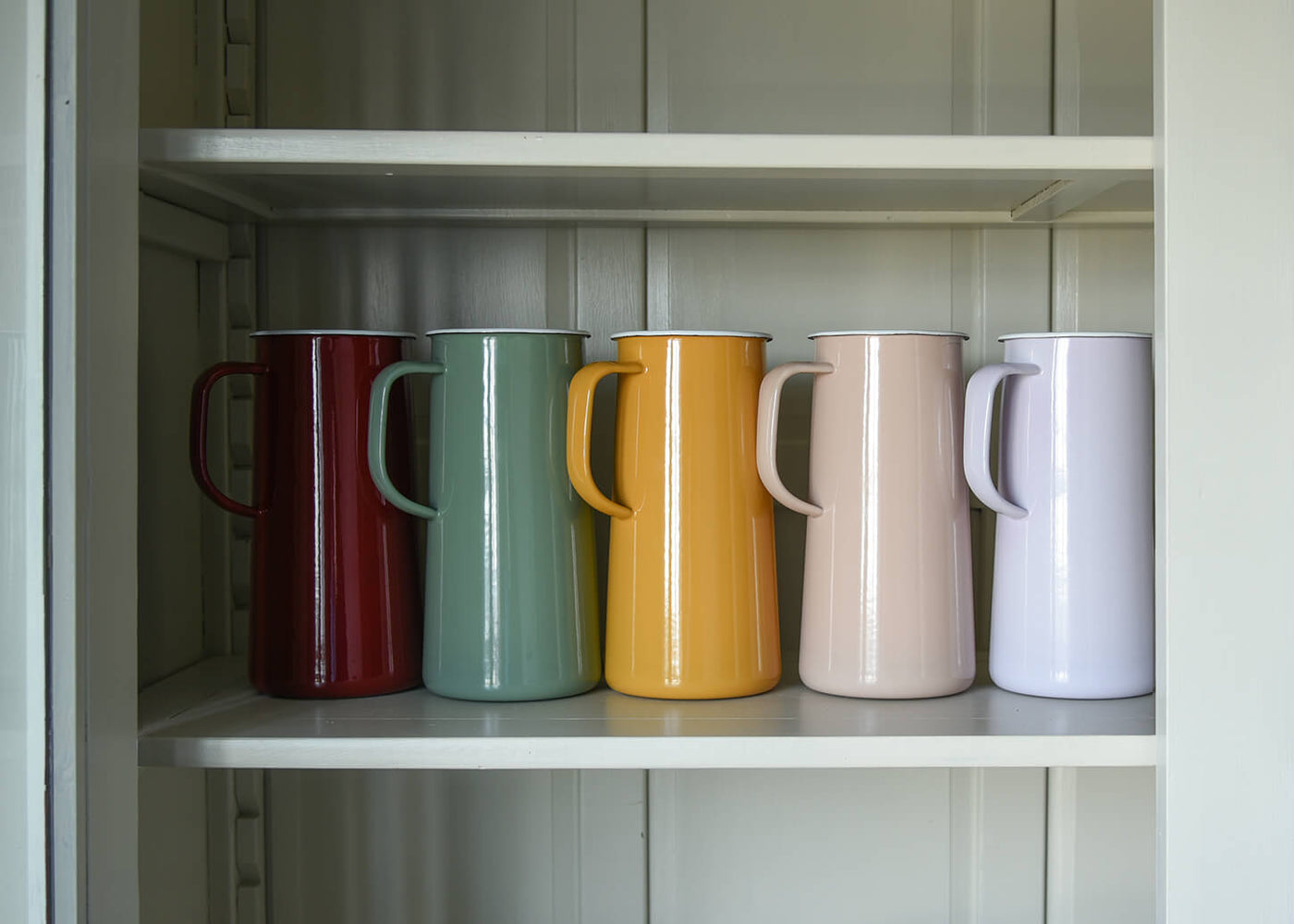 A row of colourful enamel jugs on a shelf