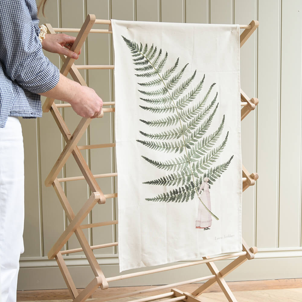 Person holding a wooden ladder with a white towel featuring fern design against a neutral wall.