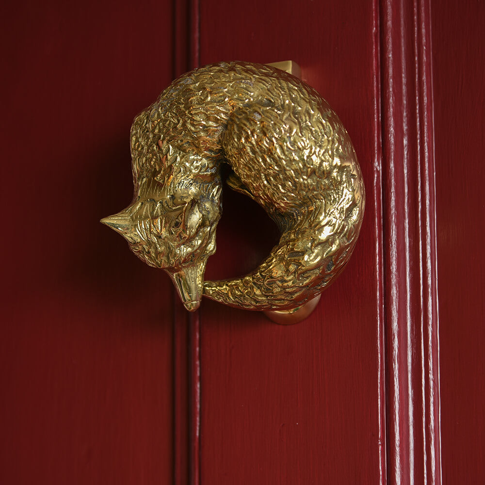 Brass fox shaped door knocker curled up asleep featured on a red door