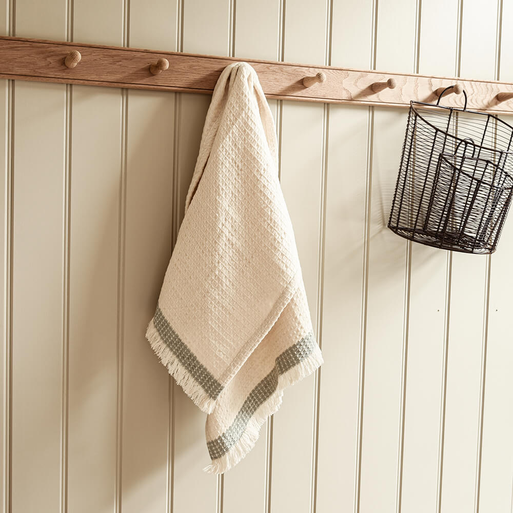 Waffle towel with a green stripe hanging on a peg rail