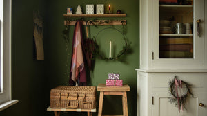Green room with light painted dresser stuffed with christmas essentials and olenty of storage. Hook rail and picture ledge are decorated with a natural garland and lights.