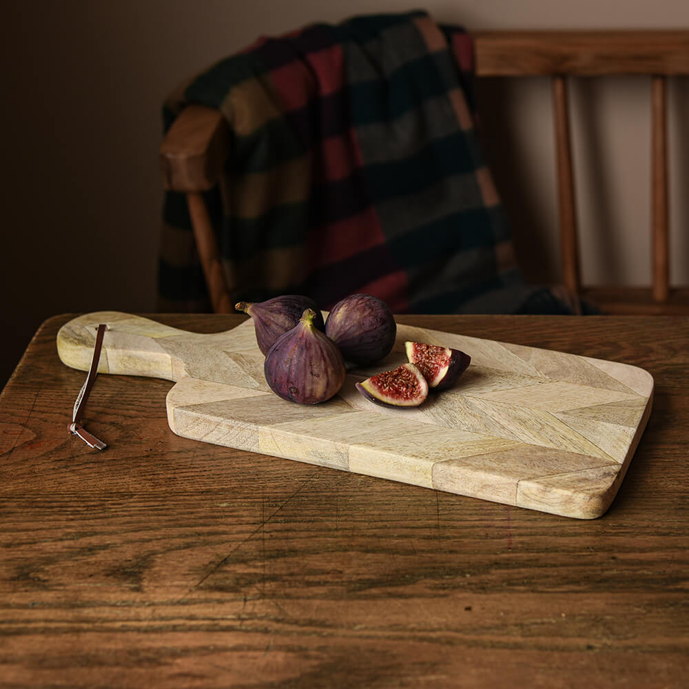 Herringbone designed wooden chopping board with figs on it, cut up on a rustic kitchen table.
