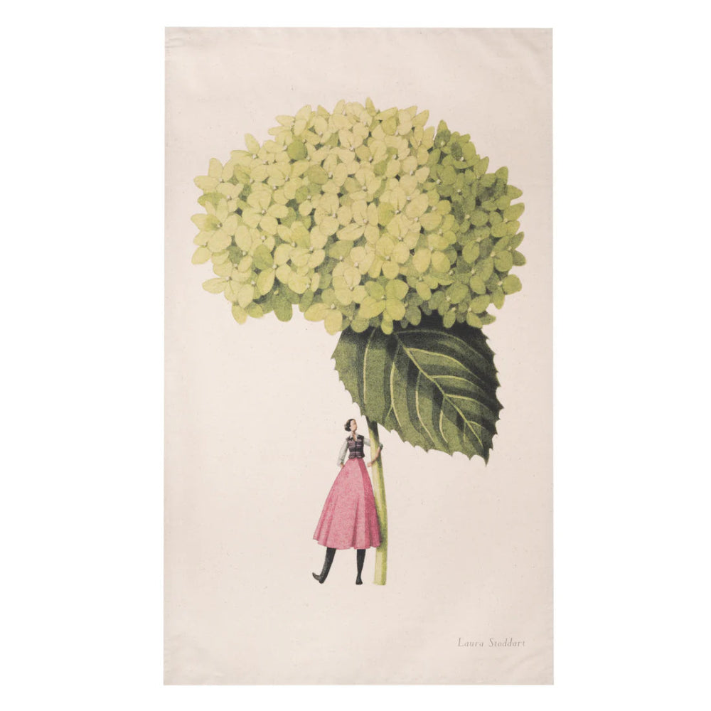 A tea towel featuring an illustration of a large green hydrangea flower with leaves, and a person in a pink dress and black shoes holding the flower.