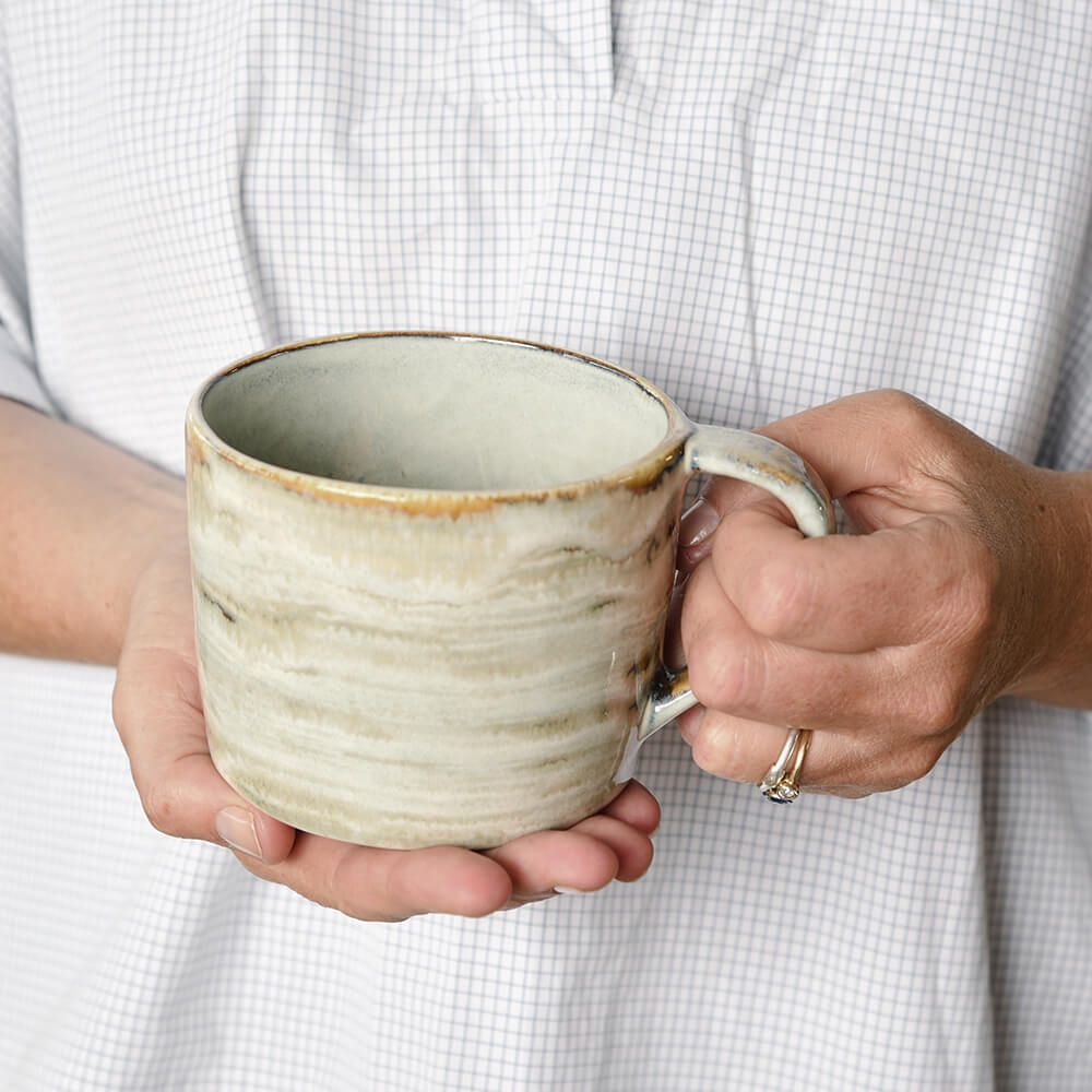 Person holding a ceramic mug with a textured surface against a neutral background