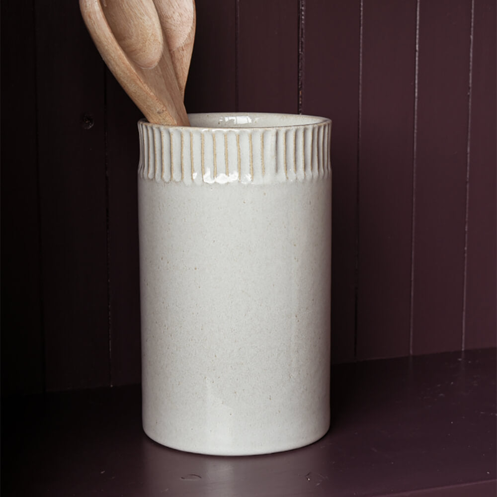 White ceramic utensil holder with wooden spoons against a dark background