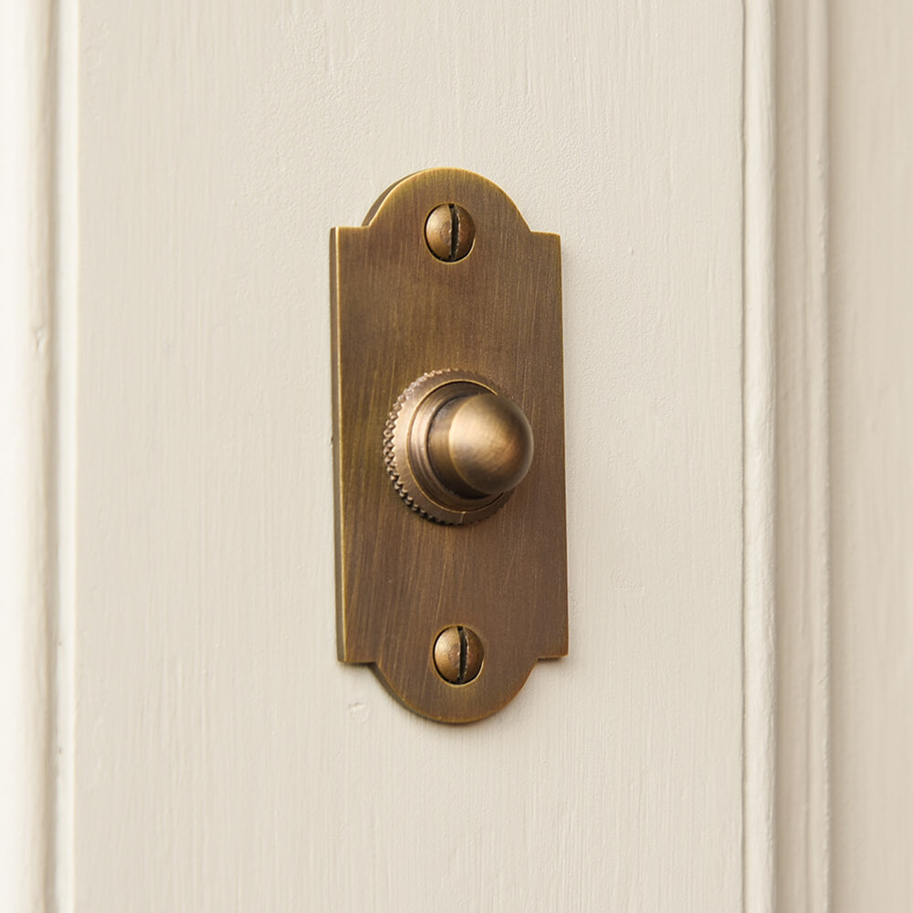 Bronze coloured brass doorbell push button on a taupe door