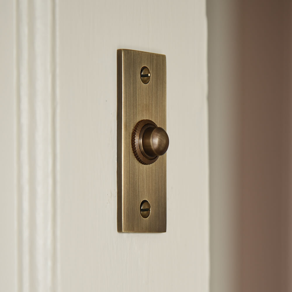 Brass bell push with a brush matt finish mounted on a cream door frame