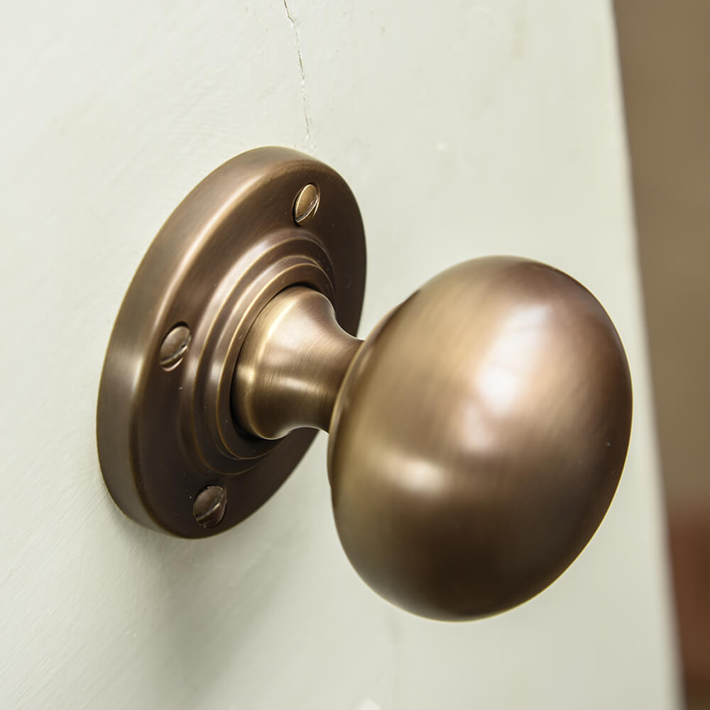 Bronze coloured door handle on a white door showing its smooth bun shaped form and reeded detail to the roseplate