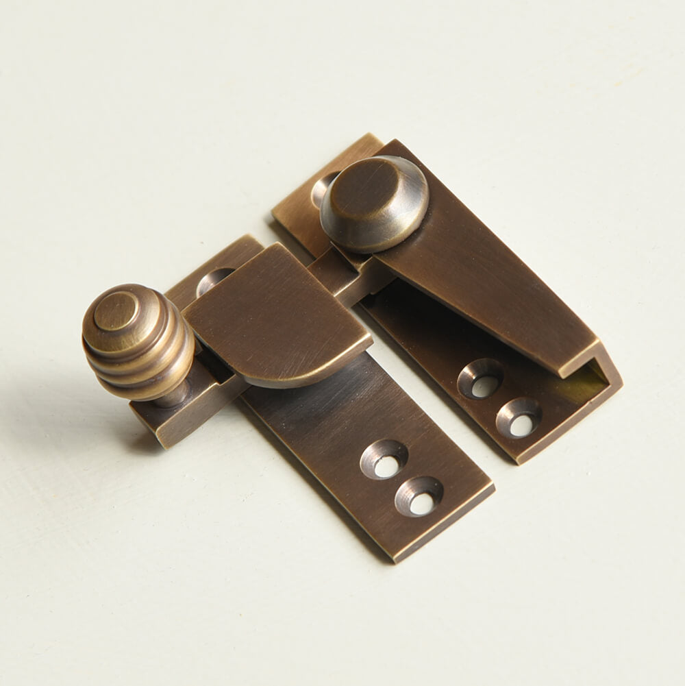 Brass window fastener on a light gray background with reeded finial