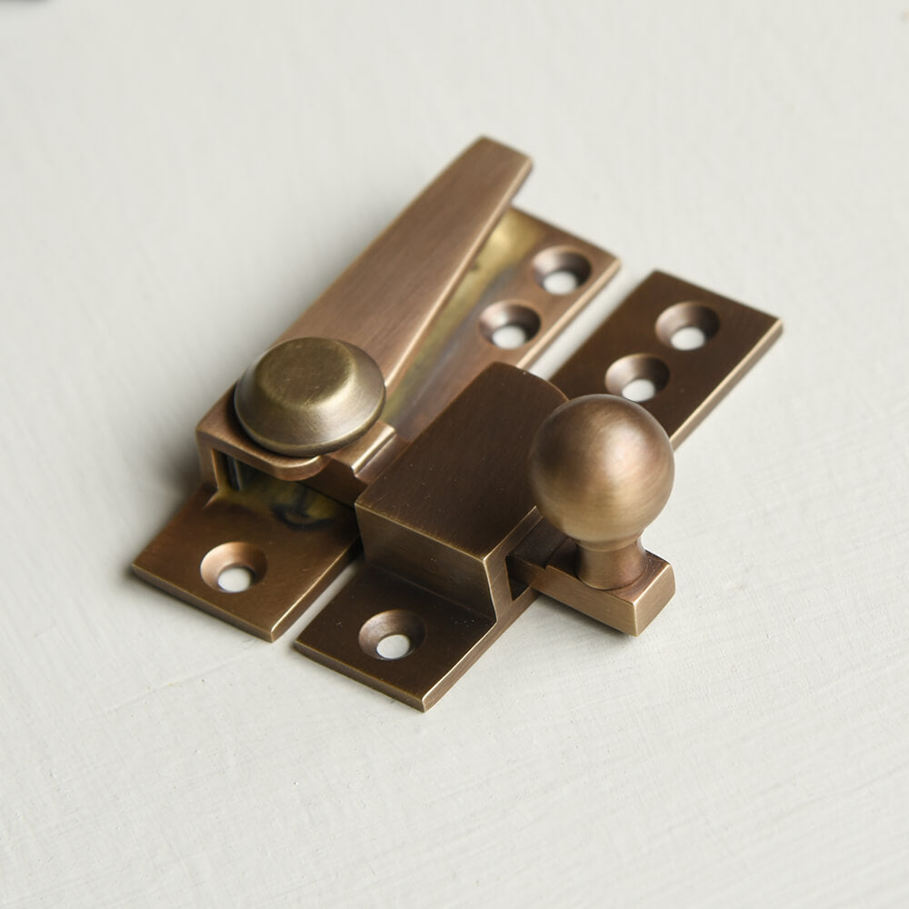 Brass window fastener on a light grey background with a ball finial