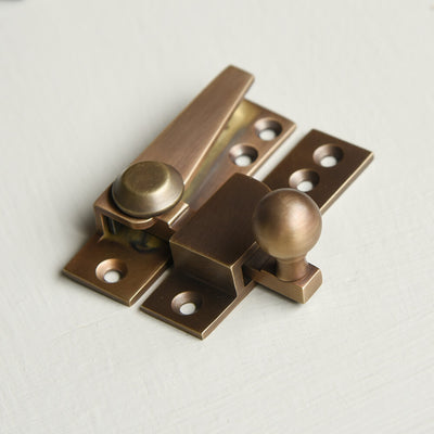 Brass window fastener on a light grey background with a ball finial