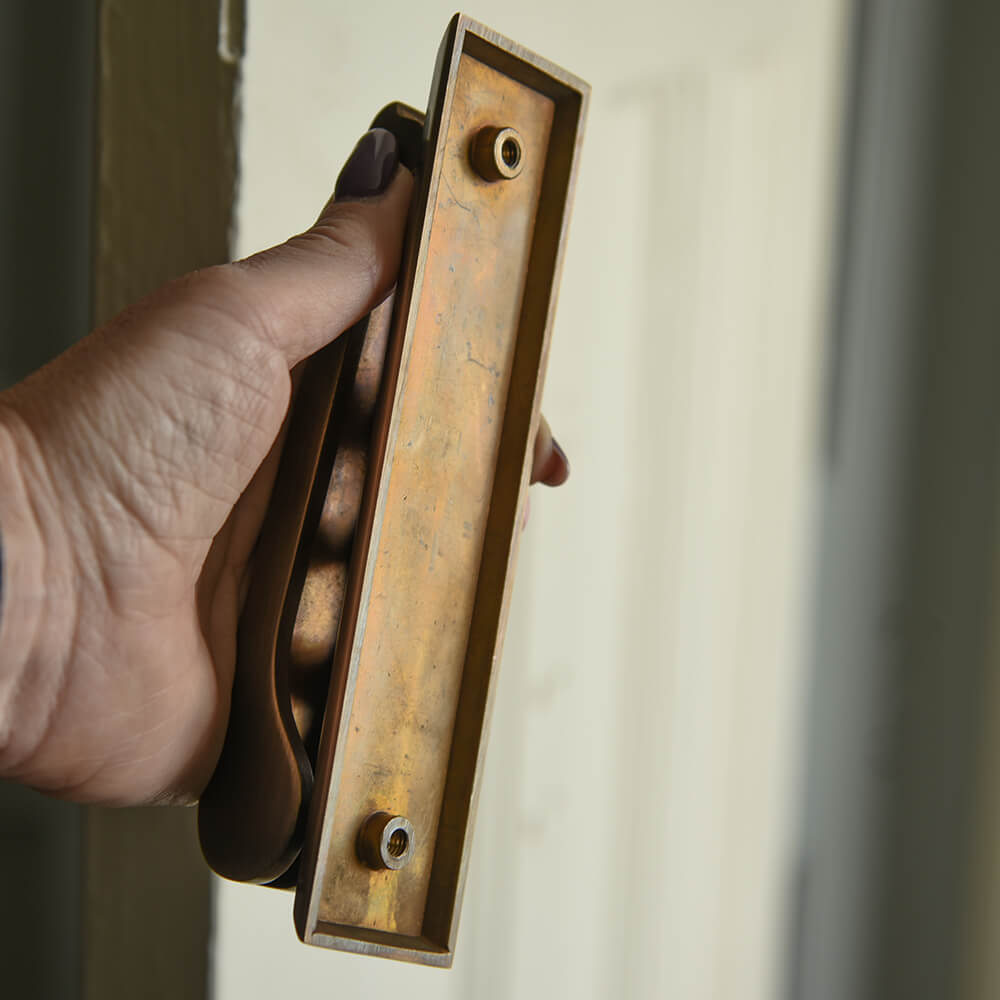 Rear view of slim brass door knocker held in a hand