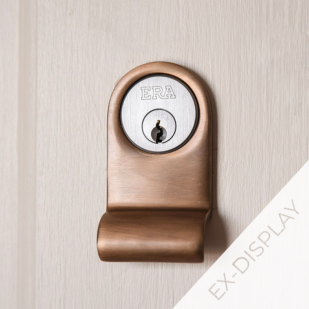 Light antique brass cylinder latch pull surrounding a yale lock on a pale pink door with a  watermark and ex display text in the corner