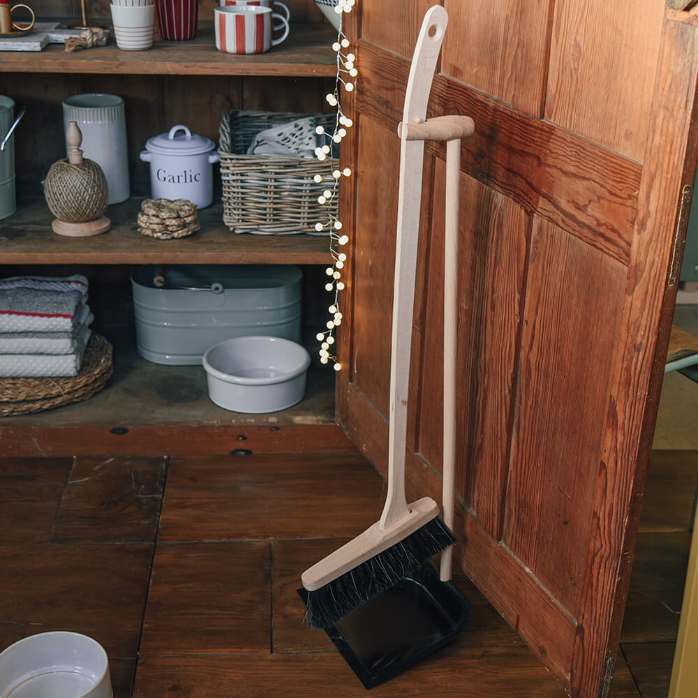 long handled brush on a pan against open cupboard with household items on shelve