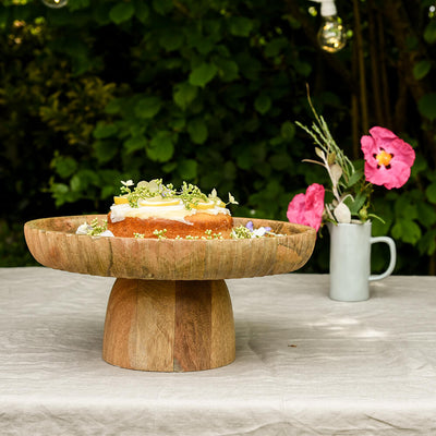 wooden cake stand in garden with lemon cake and flowers