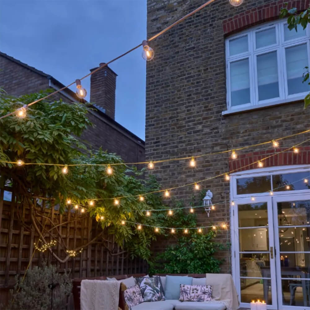 Garden patio area at dusk with coloured cable festoon lights strung above - blue, pink and yellow