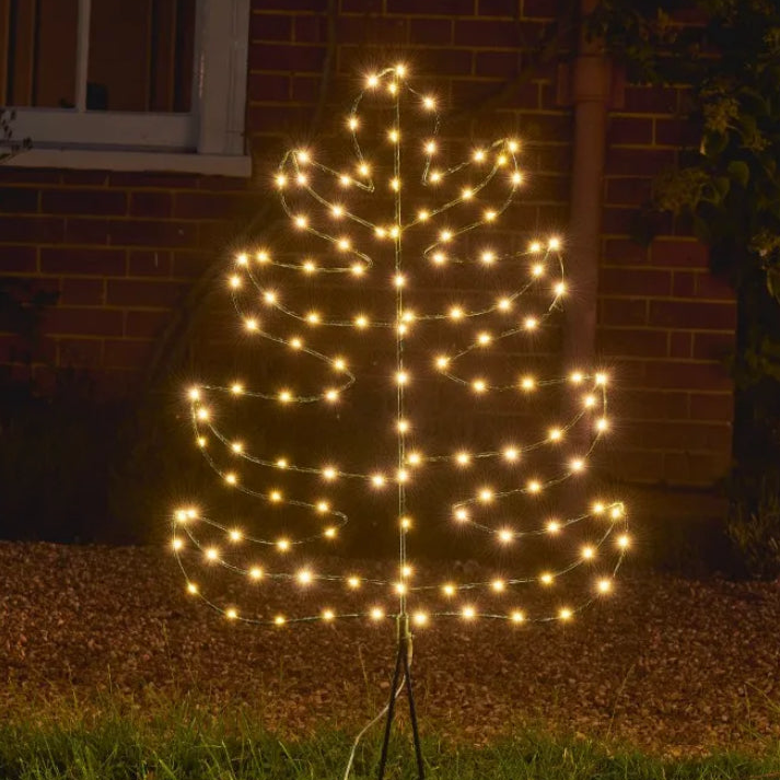 Decorative light tree with warm white lights in front of a brick wall.