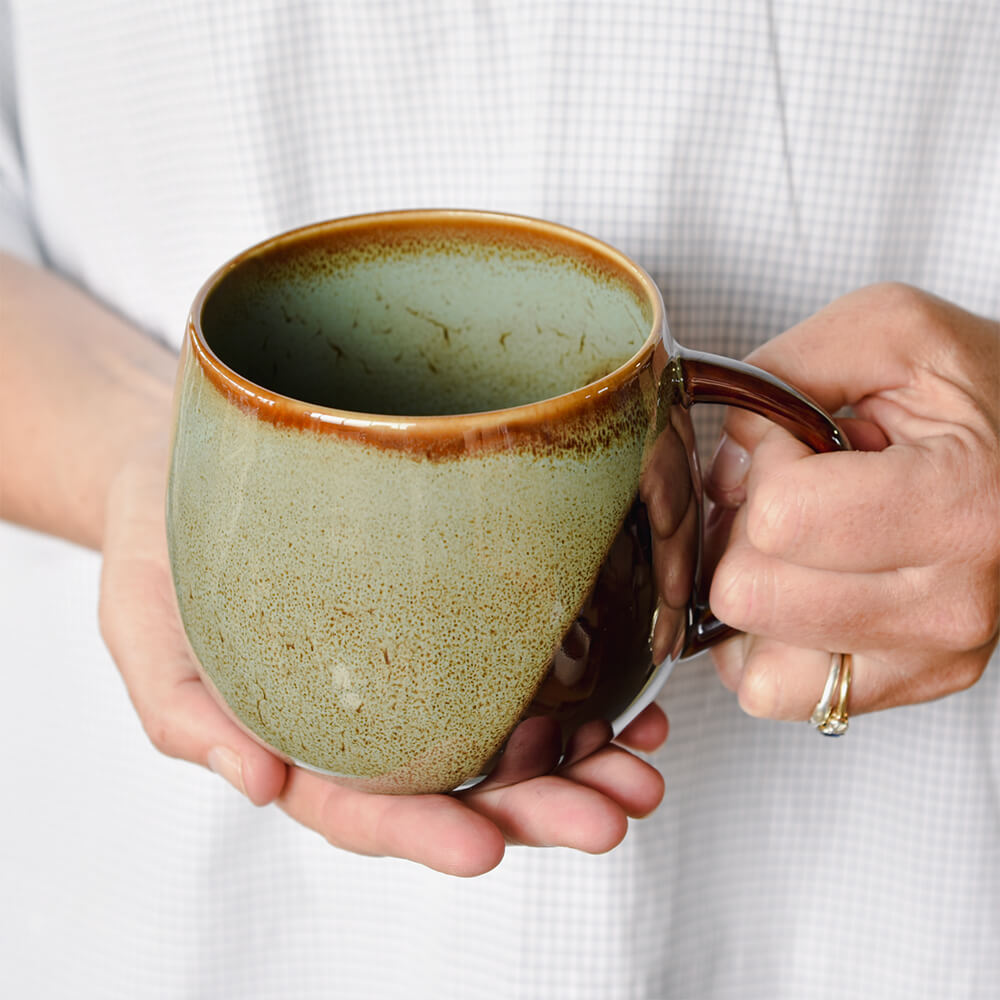 Person holding a ceramic mug with a speckled design against a white background