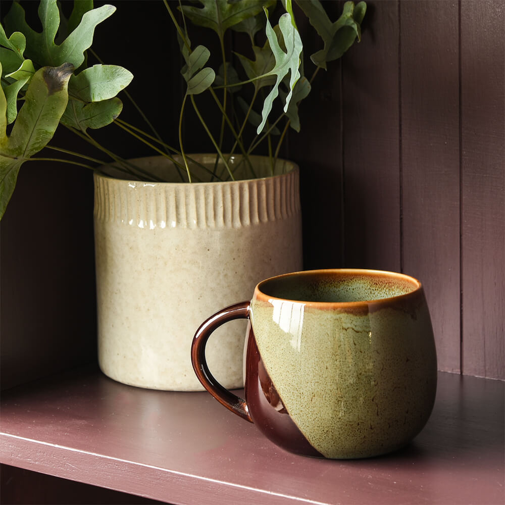 Greeny blue ceramic mug and beige pot with plants on a wooden surface