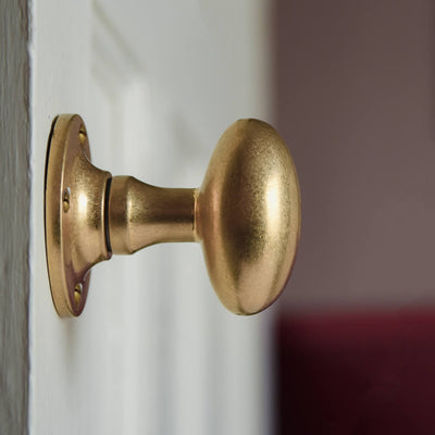 Oval aged brass door knobs on a cream door seen in profile