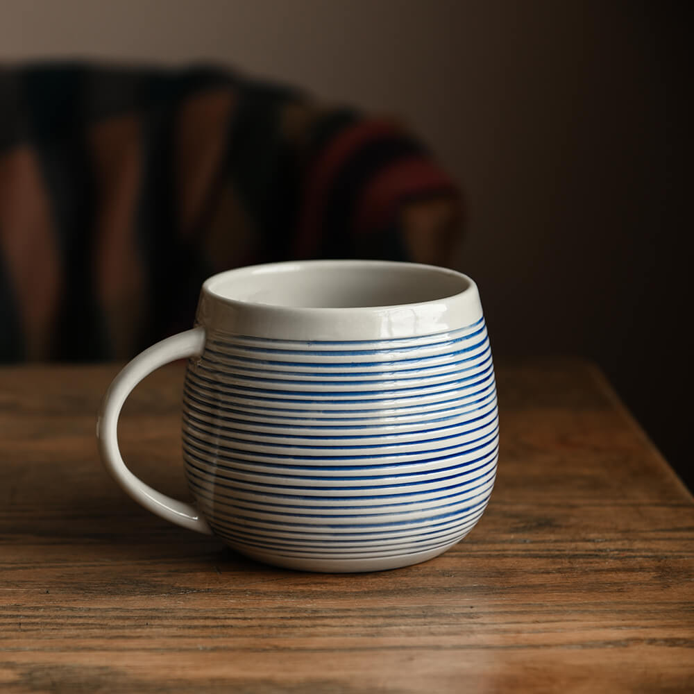 Oversized ceramic mug with blue and white horizontal stripes on a wooden table 