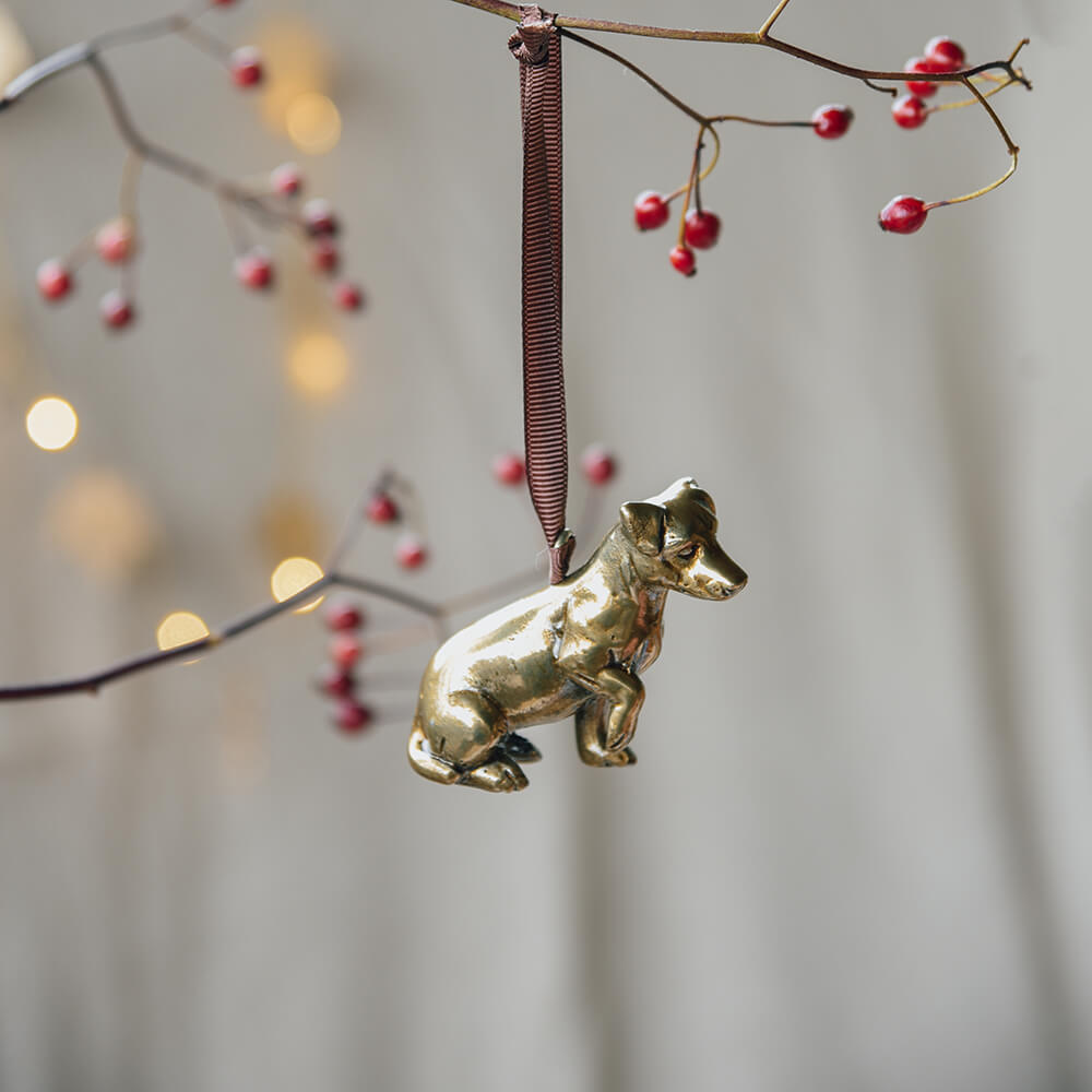 Gold dog ornament hanging from a branch with red berries and blurred lights in the background