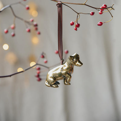 Gold dog ornament hanging from a branch with red berries and blurred lights in the background