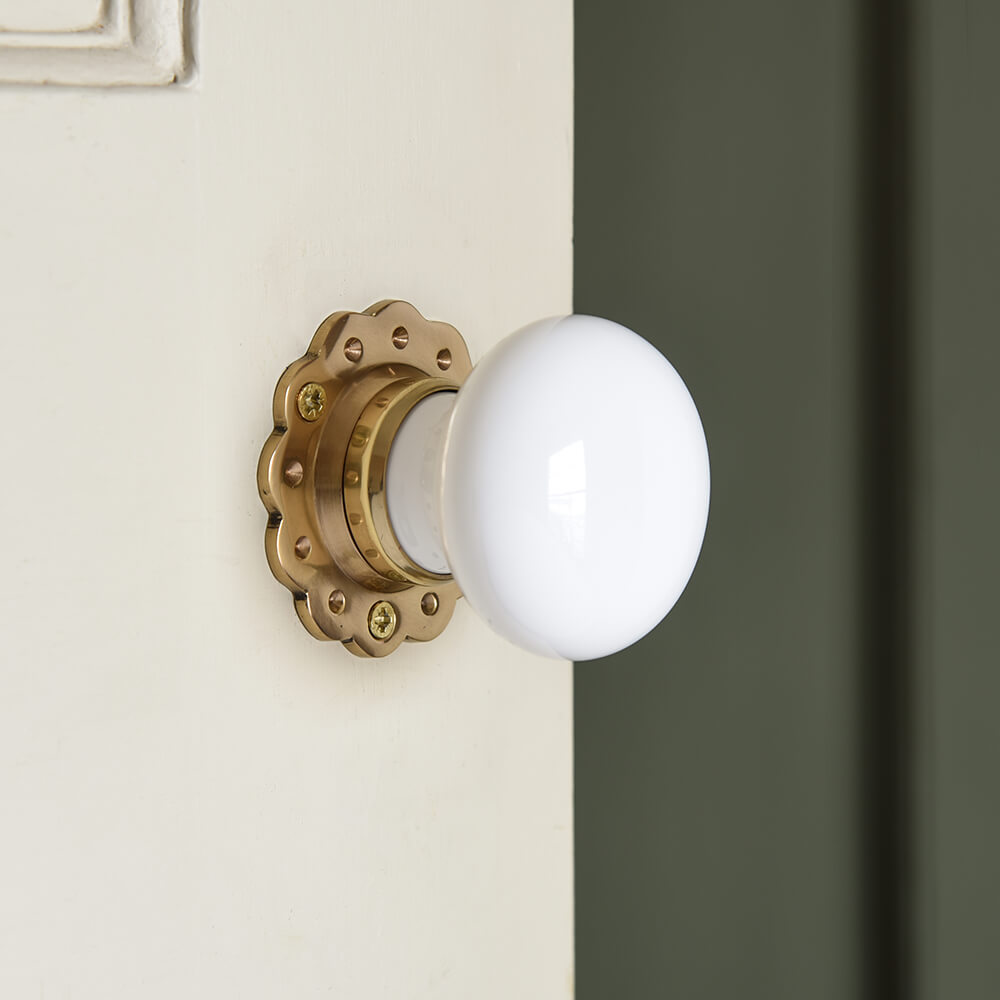 White ceramic door knobs with a brass ptal shaped backplate on a cream door against a green wall
