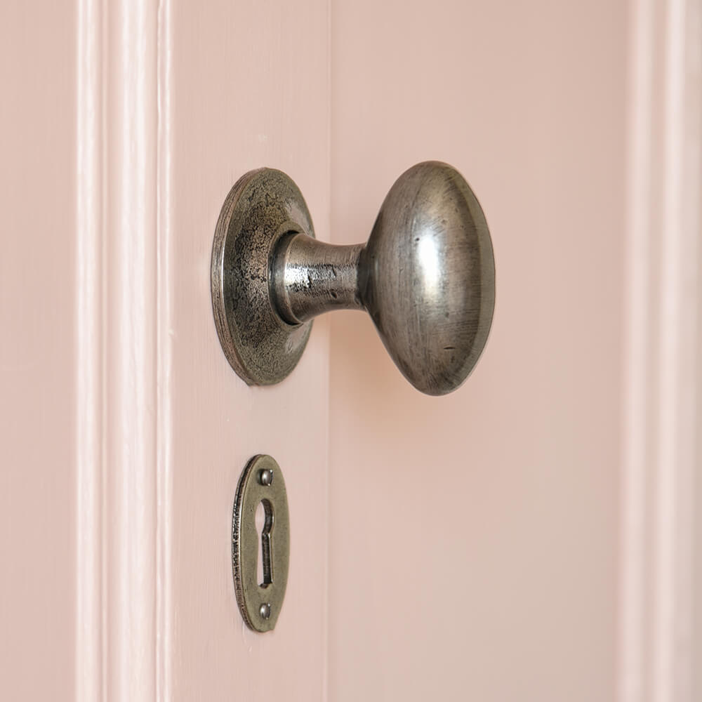 Oval door knobs and matching scutcheon in pewter on a pink door