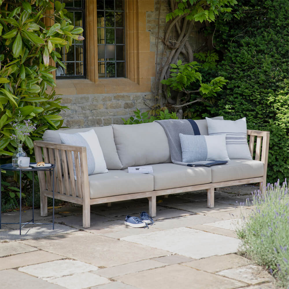 Acacia Wood Porthallow 3 Seater Sofa on a patio outside a period house with vines