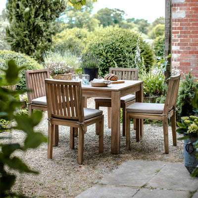 Square wooden table and four slatted chairs in a pretty garden next to a red brick wall
