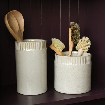 Two ceramic containers with kitchen utensils on a dark background
