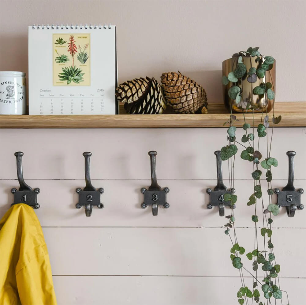 Row of iron numbered hooks with a shelf above and plant, calendar on top, yellow coat on hook