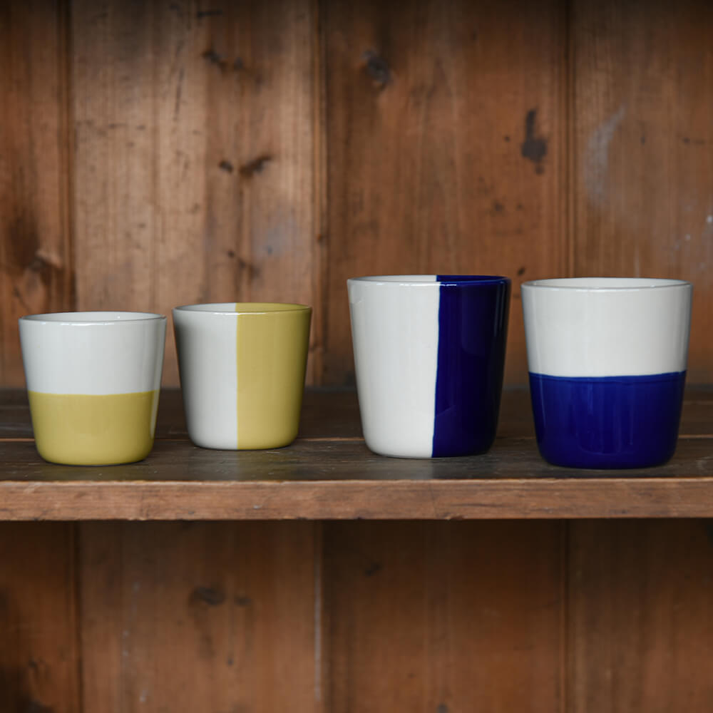 Four ceramic beakers on a shelf with bold colour glazing