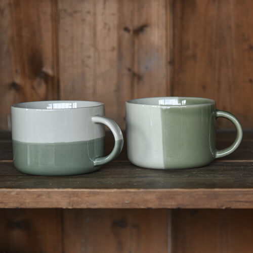 Two green ceramic mugs on a wooden surface with a wooden background