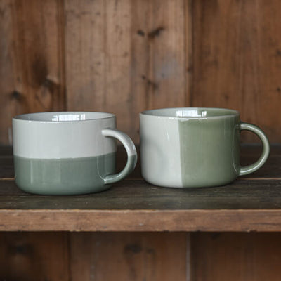 Two green ceramic mugs on a wooden surface with a wooden background