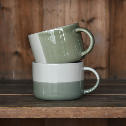 Two stacked ceramic mugs with green and white gradient on a wooden surface.