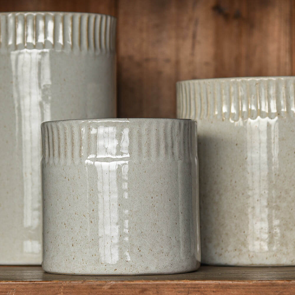 Three textured ceramic pots on a wooden surface with a wooden background