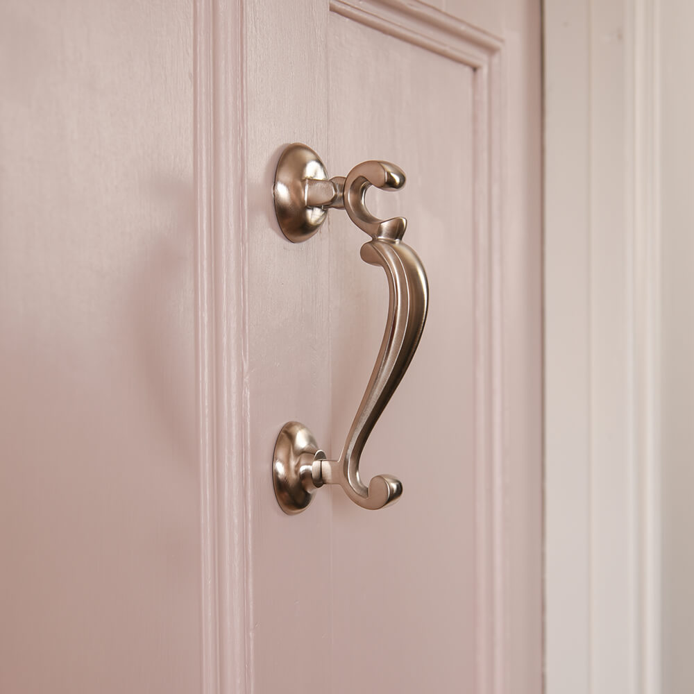 Profile shot of the satin nickel doctors door knocker on a pink door