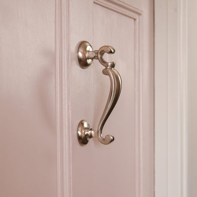 Profile shot of the satin nickel doctors door knocker on a pink door