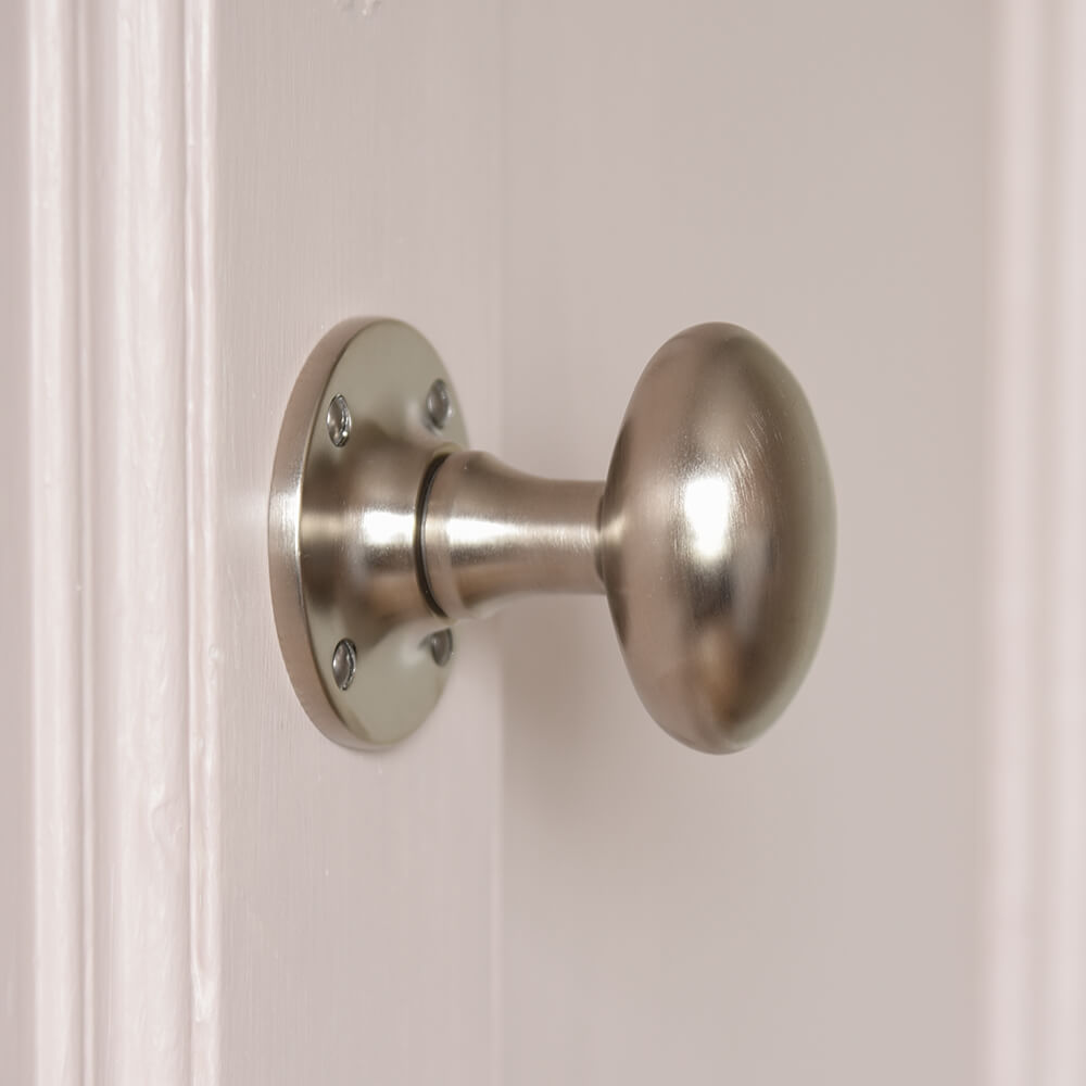 Satin nickel silver door knob in an oval shape on pale pink door