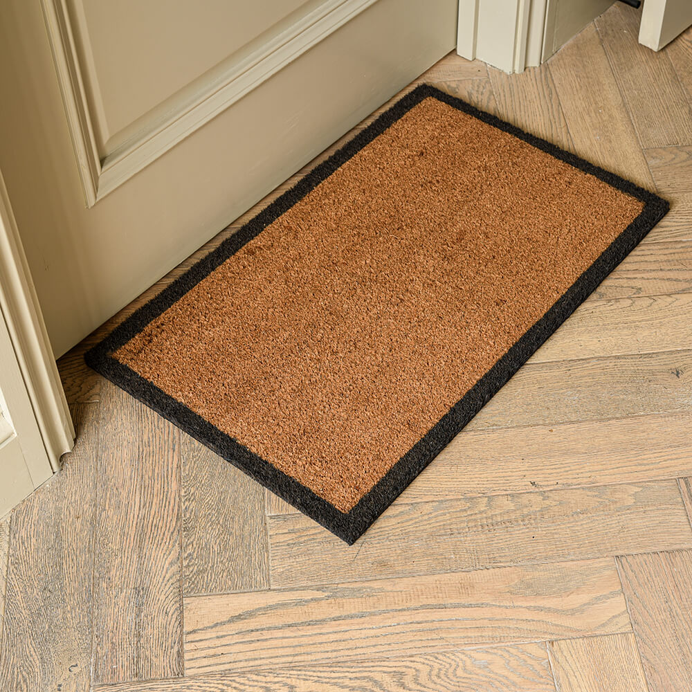 Brown doormat with black border on a wooden floor