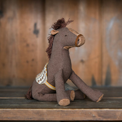 Stuffed horse toy with a saddle blanket on a wooden surface