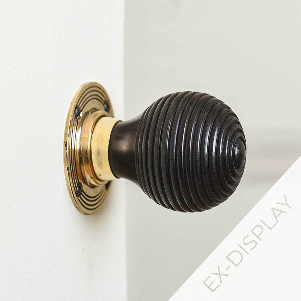 Solid ebony beehive door knob with a reeded brass backplate on a grey door with a watermark and ex display text in the corner