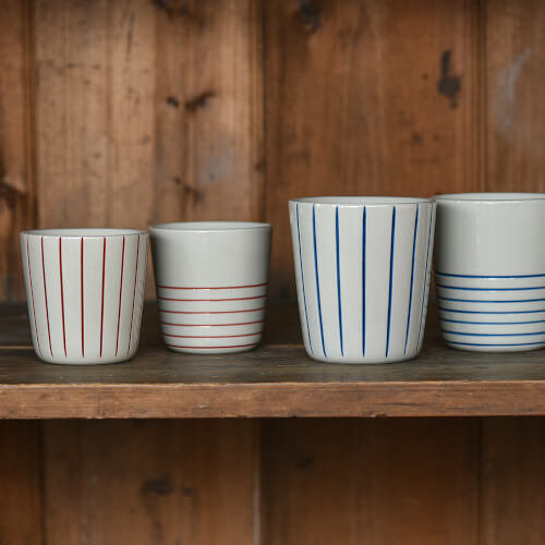 Four ceramic cups with striped patterns on a wooden shelf against a wooden wall.