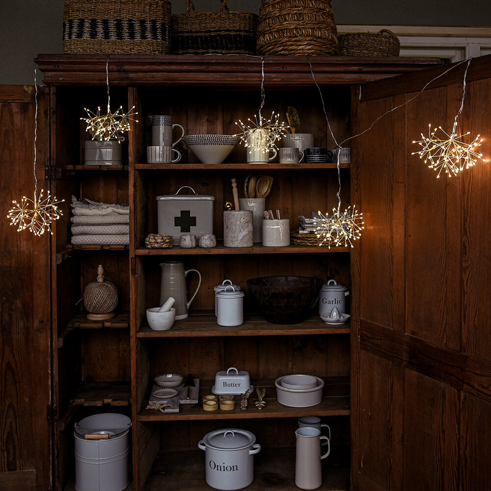 Wooden cabinet with shelves displaying various kitchen items and string lights.