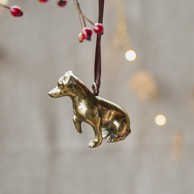 Gold dog-shaped ornament hanging from a branch with red berries against a blurred natural background.