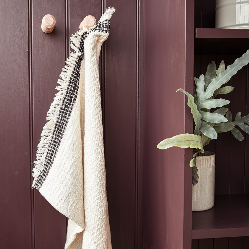 White towel with black checkered pattern hanging on a wooden cabinet with a plant in the background.